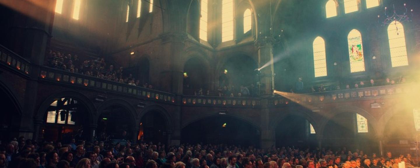 The interior of Union Chapel, dark but lit up through the round glass window behind the stage