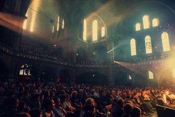 The interior of Union Chapel, dark but lit up through the round glass window behind the stage